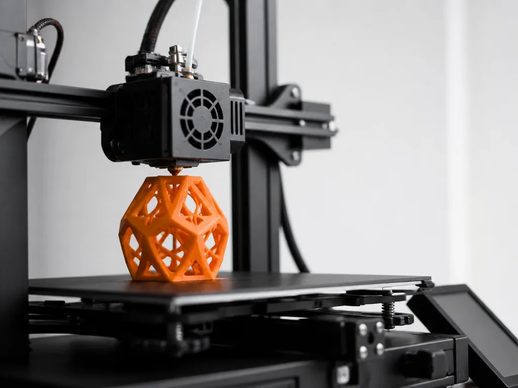 Modern 3D-skrivare med orange filament på ett välordnat hobbyskrivbord i naturligt fönsterljus